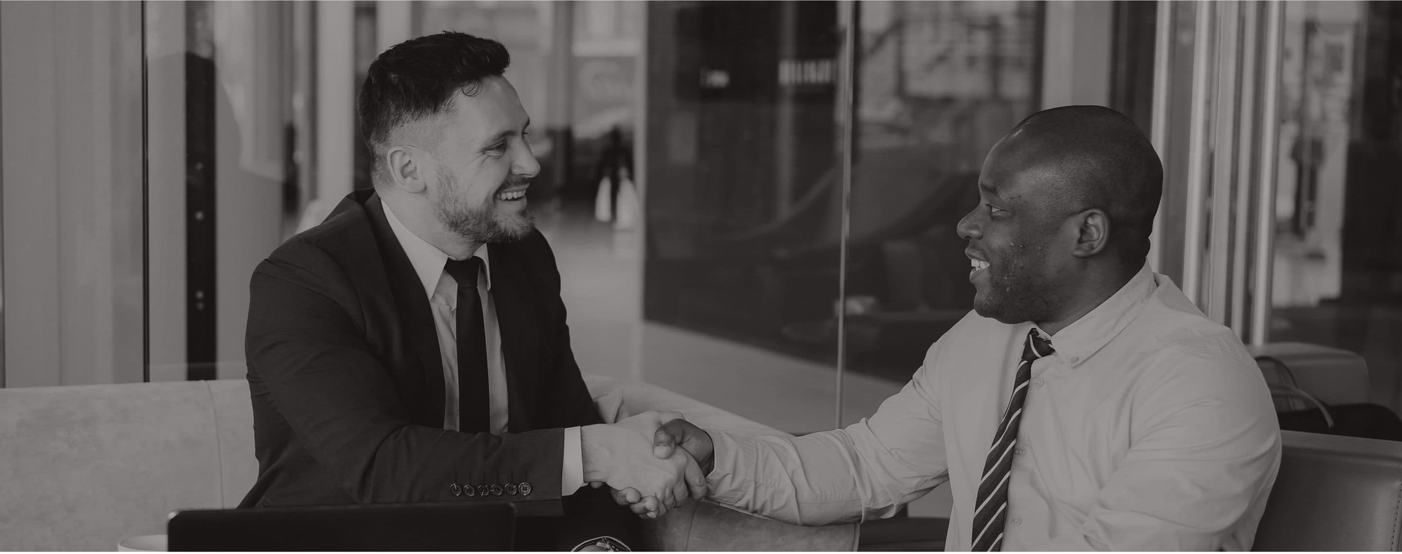 Two brokers shaking hands across a table in an office lobby